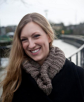 Woman in black coat and brown scarf, with water in background